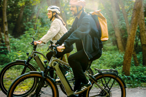 Zwei Fahrradfahrer auf einem E-Bike mit Helm von der Seite.